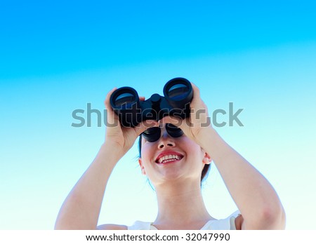 Smiling businesswoman looking through binoculars against blue sky