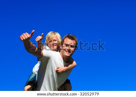 Son on father\'s back with thumbs up in a park