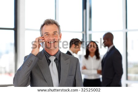 Mature businessman on phone in office with his team in the background