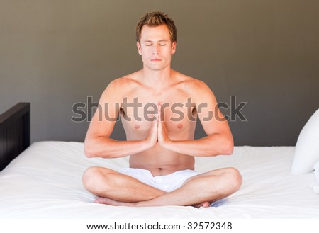 Attractive young boy doing yoga on bed with clossed eyes