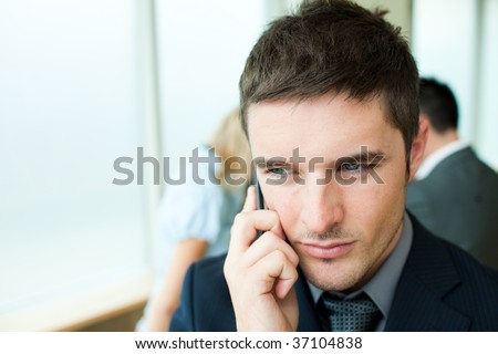 Serious businessman on phone in office with his team in the background