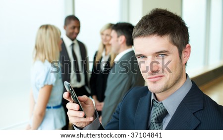 Happy businessman sending a text in office with his team in the background