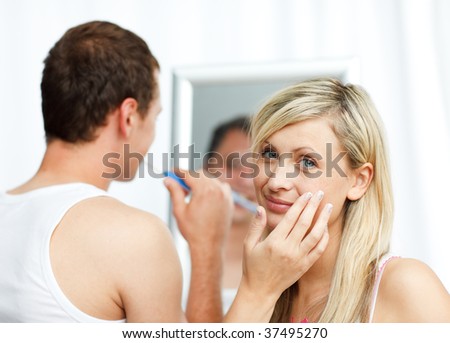 Woman putting cream on her face and man cleaning teeth in bathroom