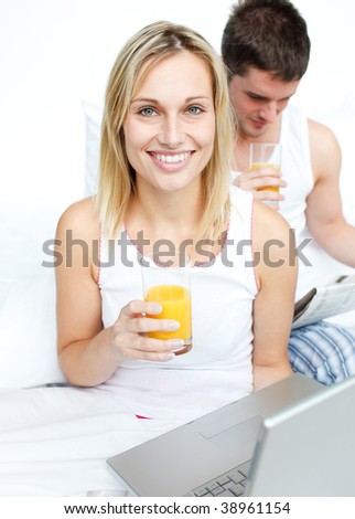 Smiling boyfriend and girlfriend drinking orange juice in bed