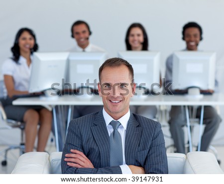 Friendly manager in call center with his team working in the background