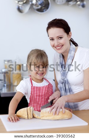 Mother teaching daughter how to cut bread in kitchen