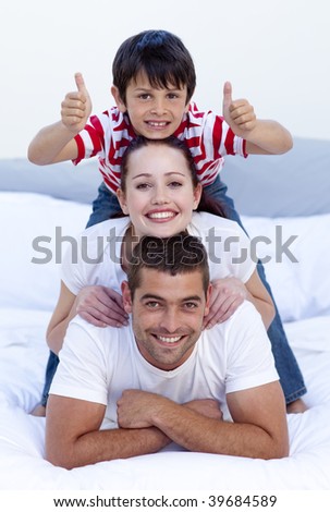 Happy parents and son playing in bed with thumbs up