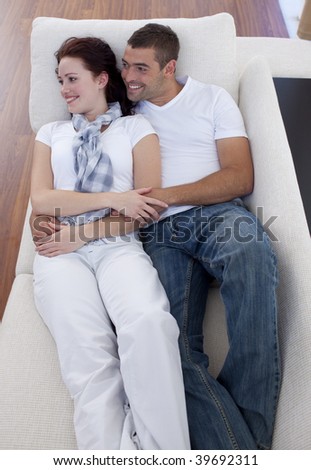 Young couple lying together on sofa watching television
