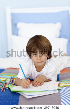 Portrait of little boy drawing in bed with colorful pencils