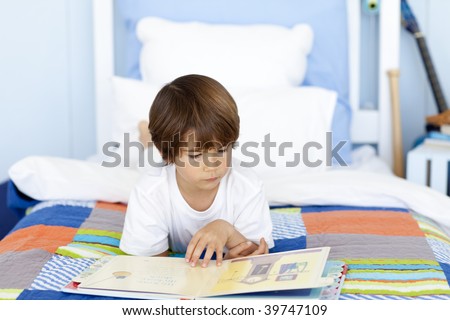 Little boy reading a book in bed