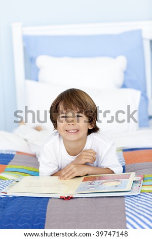 Smiling little boy reading a book in bed