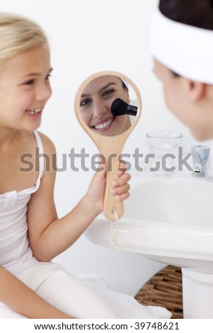 Smiling daughter holding a mirror and mother putting makeup in bathroom