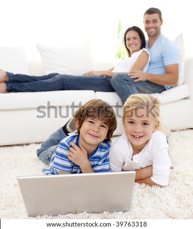 Children playing with a laptop on floor and parents lying on sofa