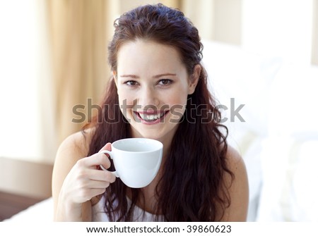 Smiling woman drinking a cup of coffee in bedroom in the morning