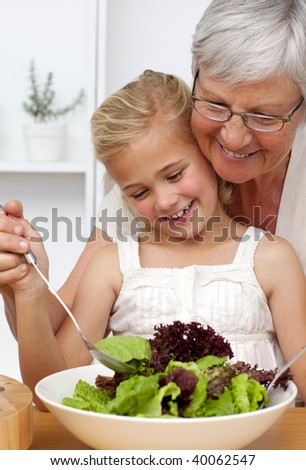 Happy grandmother cooking a salad with granddaughter in the kitchen