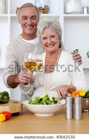 Happy senior couple eating a salad in the kitchen and drinkng wine