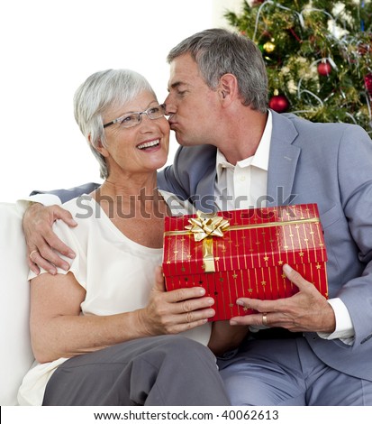 Senior man giving a kiss and a Christmas present to his wife at home