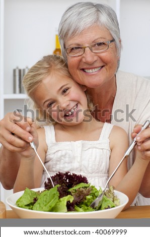Happy grandmother eating a salad with granddaughter in the kitchen