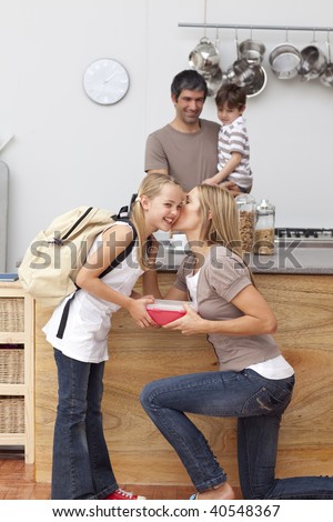 Mother giving her daughter the school lunch and a kiss in the kitchen