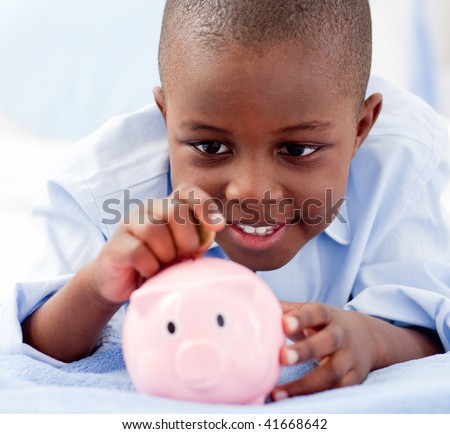 Young Boy lying on his bed putting money into a piggy bank