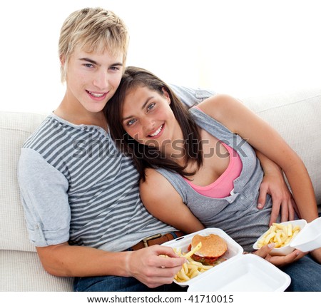 stock photo Teen couple eating burgers and fries on the sofa at home