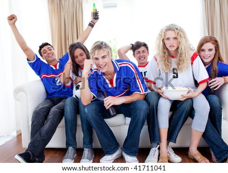 Excited and happy teenagers watching a football match in the living-room