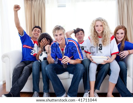 Group of excited and happy teenagers watching a football match in the living-room