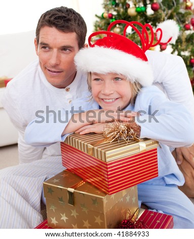 Smiling father and his son holding Christmas gifts and sitting on the floor