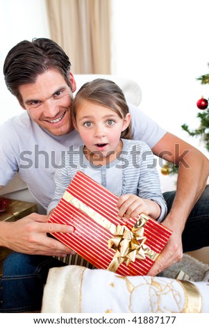 Portrait of a surprised little girl with her father holding a Christmas present