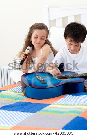 Brother and sister having fun with a guitar in the bedroom