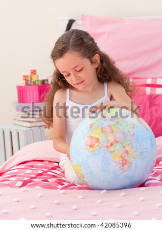 Little girl having fun with a terrestrial globe in the bedroom