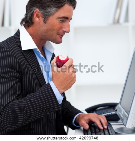 Close-up of a happy businessman eating a red apple in the office