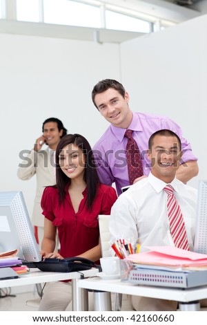 International business team smiling at the camera with their manager on phone in the background