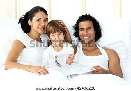 Smiling parents and their son looking at the camera on the bed