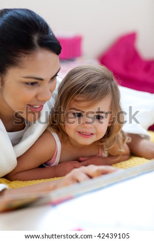 Caring mother reading a book with her girl in the bedroom