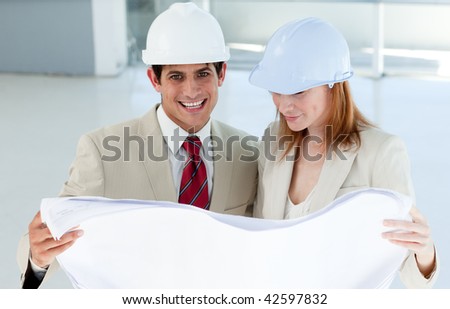 Two smiling engineers studying blueprints in a building site