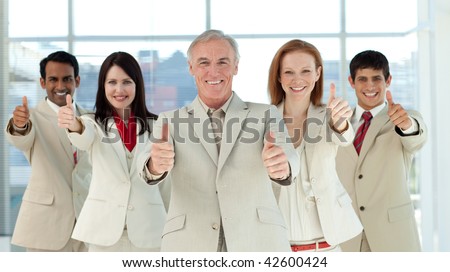 Smiling multi-ethnic business team with thumbs up in a business building