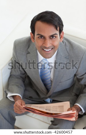 Smiling businessman reading a newspaper and sitting in a waiting room