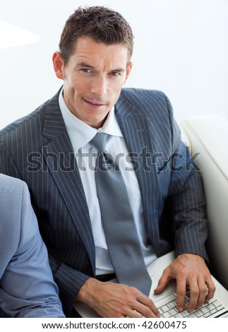 Smiling businessman using a laptop and sitting in a waiting room