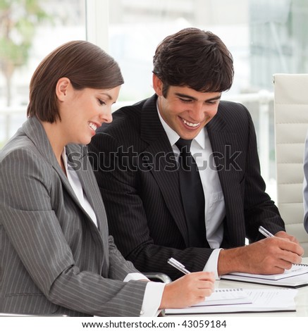 Two smiling colleagues studying sales report with their team in a meeting