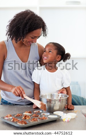 Happy mother helping her daughter cooking biscuits in the kitchen