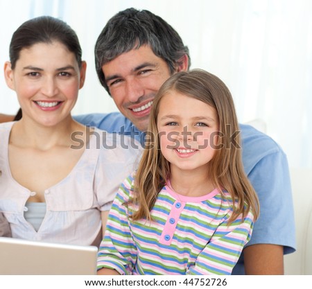 Little girl using a laptop with her parents on the sofa