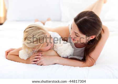 Jolly mother talking with her little girl lying on a bed
