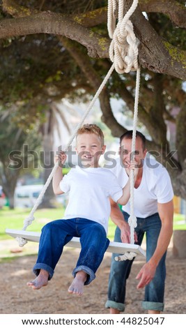 Happy daddy pushing his son on a swing