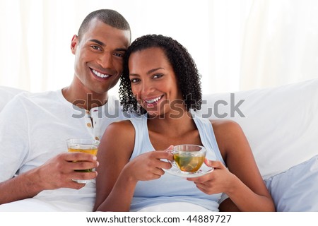Smiling couple drinking a cup of tea on their bed. Concept of love.