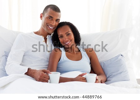 Smiling Afro-american couple drinking a coffee on their bed