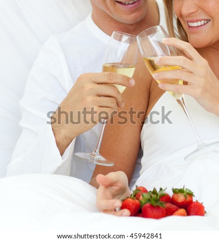 Close-up of a couple drinking Champagne with strawberries lying on their bed