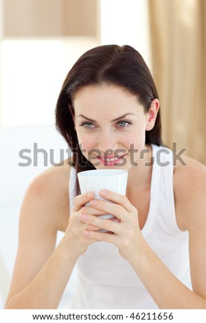 Radiant woman drinking a coffee sitting on her bed