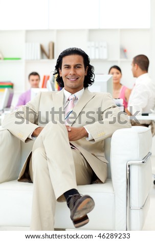 Confident manager sitting in an armchair in front of his team in the office