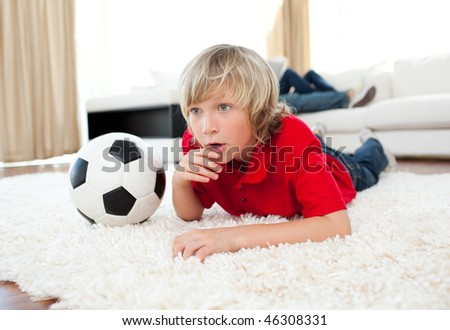 Animated boy watching football match lying on the floor in the living-room